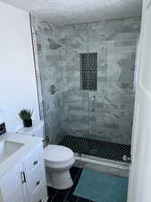 Bathroom featuring vanity, tile patterned flooring, toilet, a textured ceiling, and walk in shower