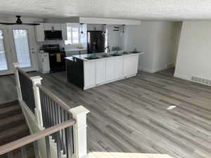 Kitchen featuring ceiling fan, refrigerator with ice dispenser, electric range, a center island with sink, and white cabinets