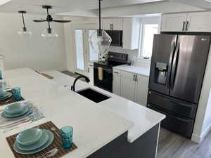 Kitchen with sink, stainless steel refrigerator with ice dispenser, black electric range, decorative light fixtures, and white cabinetry