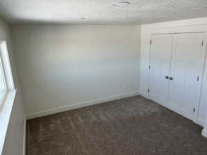 Unfurnished bedroom featuring dark carpet, a textured ceiling, and a closet