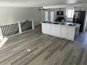 Kitchen with dark hardwood / wood-style flooring, a textured ceiling, stainless steel fridge with ice dispenser, black electric range oven, and an island with sink