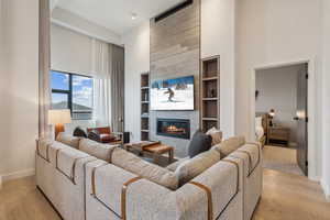 Living room with built in shelves, light hardwood / wood-style floors, a high ceiling, and a tiled fireplace