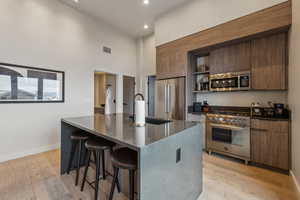 Kitchen featuring high quality appliances, a center island with sink, a kitchen breakfast bar, sink, and light hardwood / wood-style floors