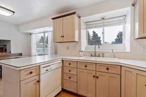 Kitchen featuring kitchen peninsula, backsplash, white dishwasher, sink, and light brown cabinets