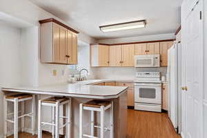 Kitchen featuring kitchen peninsula, light brown cabinets, white appliances, and a breakfast bar