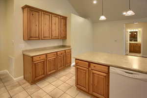 Kitchen with white dishwasher, decorative light fixtures, light tile patterned flooring, and vaulted ceiling