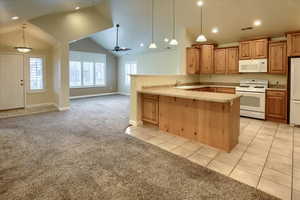 Kitchen with pendant lighting, white appliances, light carpet, vaulted ceiling, and kitchen peninsula