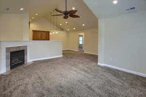 Unfurnished living room featuring ceiling fan, carpet floors, high vaulted ceiling, and a tiled fireplace