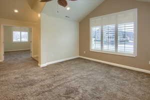 Carpeted spare room featuring vaulted ceiling and ceiling fan