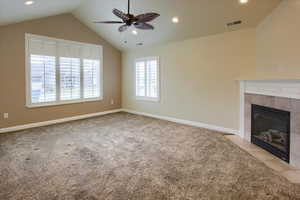 Unfurnished living room with ceiling fan, a fireplace, light colored carpet, and vaulted ceiling