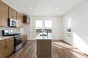 Kitchen featuring light stone countertops, sink, stainless steel appliances, dark hardwood / wood-style flooring, and a center island with sink