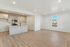 Kitchen featuring appliances with stainless steel finishes, backsplash, a kitchen island with sink, light hardwood / wood-style floors, and white cabinetry