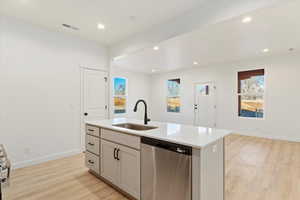 Kitchen with stainless steel dishwasher, light hardwood / wood-style floors, sink, and an island with sink