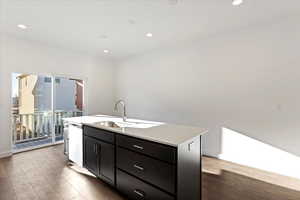 Kitchen featuring hardwood / wood-style floors, dishwashing machine, sink, and an island with sink