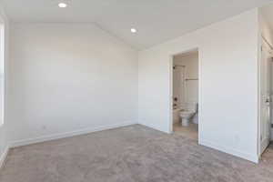 Unfurnished bedroom featuring ensuite bathroom, lofted ceiling, and light carpet