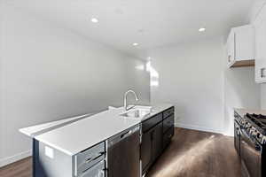 Kitchen with sink, dark hardwood / wood-style flooring, a kitchen island with sink, white cabinets, and appliances with stainless steel finishes