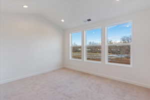 Empty room featuring light carpet and vaulted ceiling