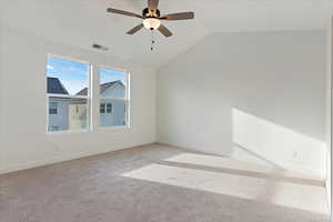 Carpeted spare room featuring ceiling fan and vaulted ceiling