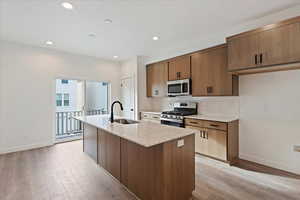 Kitchen with light hardwood / wood-style floors, sink, stainless steel appliances, and an island with sink