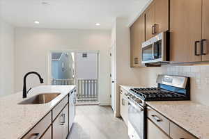 Kitchen featuring sink, decorative backsplash, light stone countertops, light hardwood / wood-style floors, and stainless steel appliances