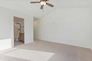 Unfurnished bedroom with ensuite bathroom, ceiling fan, light colored carpet, and lofted ceiling