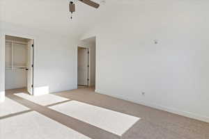 Unfurnished bedroom with ceiling fan, a closet, light carpet, and vaulted ceiling