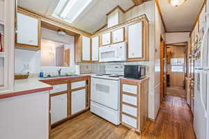 Kitchen with vaulted ceiling, sink, white cabinets, and white appliances