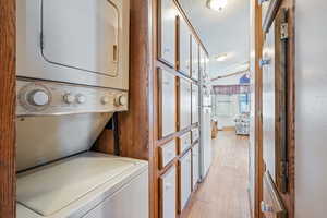 Laundry area featuring light wood-type flooring, a textured ceiling, and stacked washer and clothes dryer