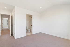 Unfurnished bedroom featuring lofted ceiling, light carpet, and connected bathroom