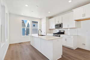 Kitchen with white cabinets, appliances with stainless steel finishes, sink, and an island with sink