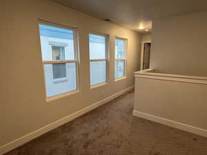 Hallway featuring dark colored carpet and a textured ceiling