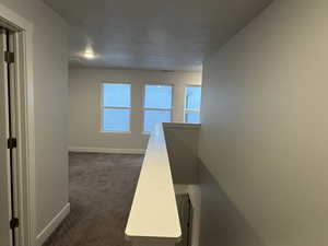 Hallway featuring dark colored carpet and a textured ceiling