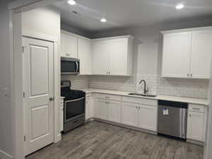 Kitchen with backsplash, dark wood-type flooring, sink, white cabinetry, and stainless steel appliances