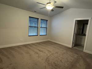 Unfurnished bedroom featuring ceiling fan, carpet floors, ensuite bathroom, and lofted ceiling