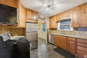 Kitchen featuring light stone countertops, appliances with stainless steel finishes, backsplash, and sink