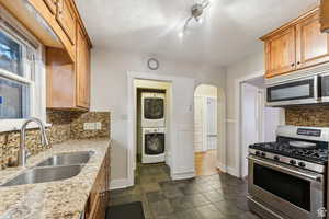 Kitchen featuring sink, decorative backsplash, stacked washing maching and dryer, appliances with stainless steel finishes, and light stone counters