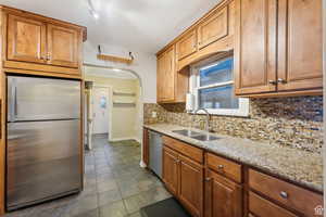 Kitchen featuring tasteful backsplash, light stone countertops, sink, and appliances with stainless steel finishes