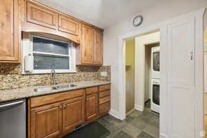 Kitchen with tasteful backsplash, stainless steel dishwasher, stacked washer and clothes dryer, and sink