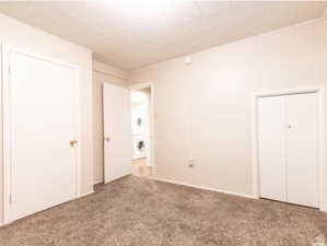 Unfurnished bedroom featuring stacked washer / dryer and light colored carpet