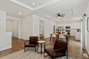 Living room with a tray ceiling, ceiling fan, sink, and light wood-type flooring