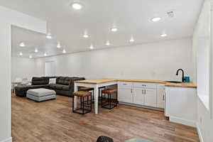 Kitchen featuring butcher block counters, sink, light hardwood / wood-style flooring, white cabinetry, and a breakfast bar area