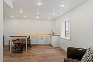 Kitchen featuring butcher block counters, white cabinetry, light hardwood / wood-style flooring, and sink