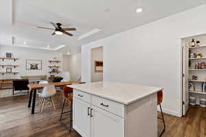 Kitchen with a kitchen bar, a raised ceiling, dark wood-type flooring, white cabinets, and a center island