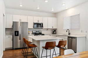 Kitchen with appliances with stainless steel finishes, a kitchen breakfast bar, sink, white cabinets, and a kitchen island