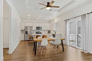 Dining area with a tray ceiling, light hardwood / wood-style flooring, ceiling fan, and sink