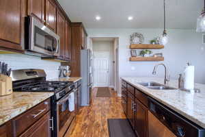 Kitchen with backsplash, hanging light fixtures, sink, appliances with stainless steel finishes, and dark hardwood / wood-style flooring