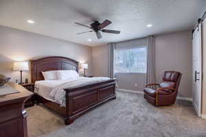 Carpeted bedroom with a textured ceiling, a barn door, and ceiling fan