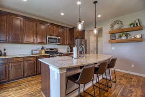 Kitchen featuring a kitchen bar, stainless steel appliances, light stone countertops, and a center island with sink