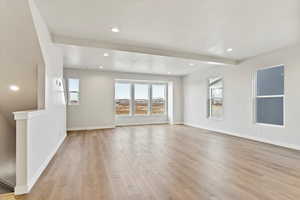 Unfurnished living room with beamed ceiling, a textured ceiling, and light wood-type flooring