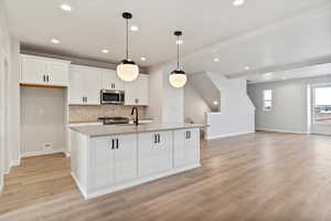 Kitchen with white cabinetry, hanging light fixtures, a center island with sink, light wood-type flooring, and decorative backsplash